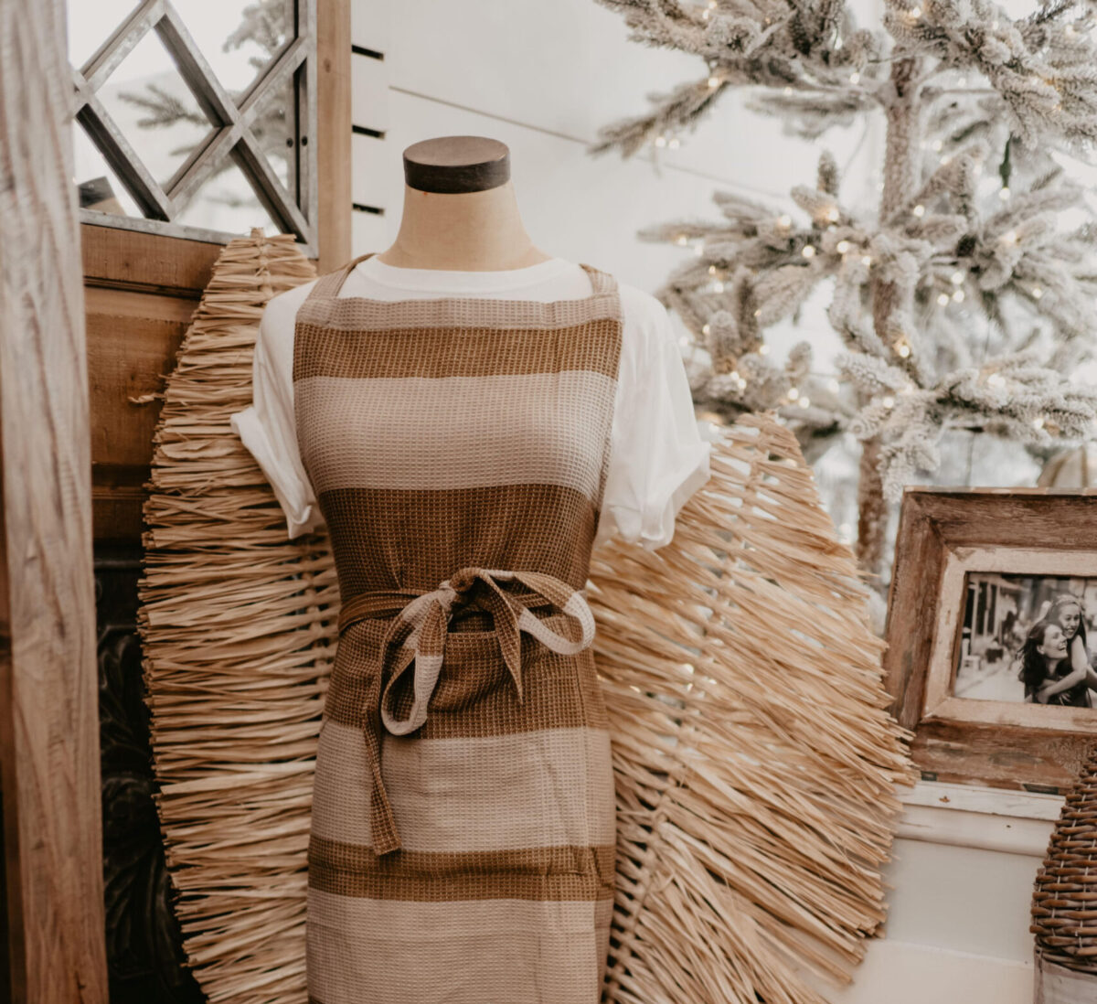 Store display with a mannequin wearing a brown striped apron next to decorative pillows and other home goods