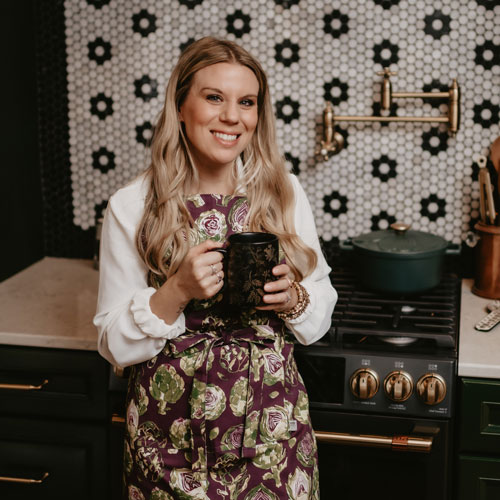 Chelsea standing with a cup of coffee in front of a stove
